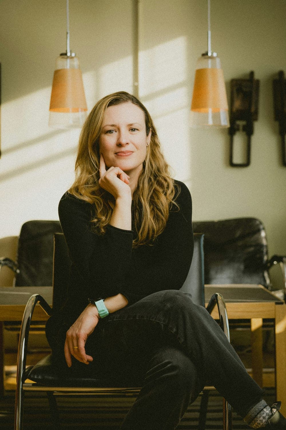 A coach in black sitting in a leather armchair, her hand under her chin