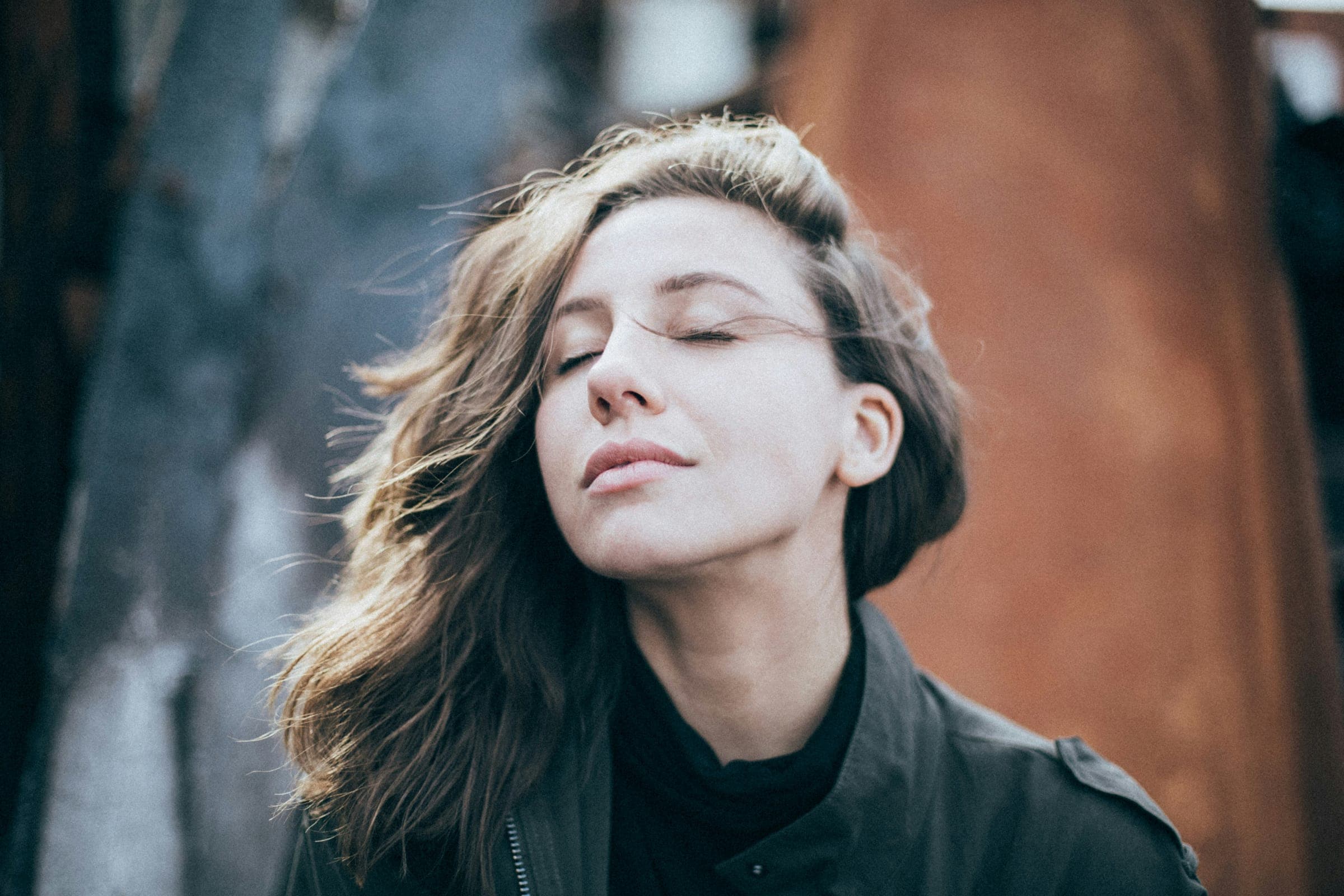 A woman with her eyes closed and her face lifted, wind in her long hair