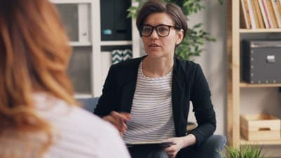 A woman with glasses in a black blazer taking notes