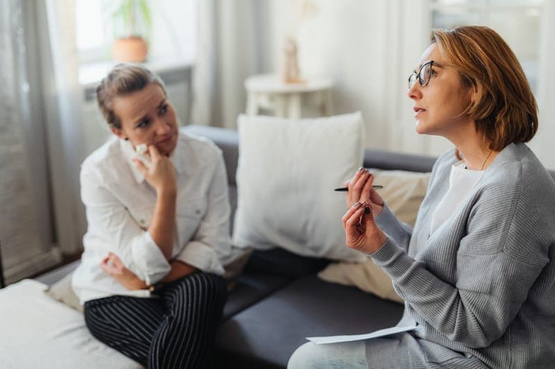 Two women talking on a sofa in a bright living room