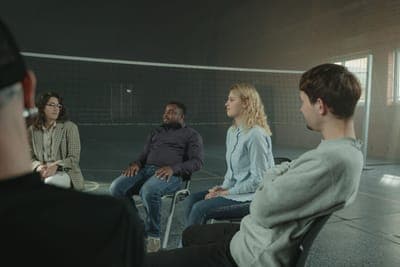 A group talking in a circle of chairs in a dim hall