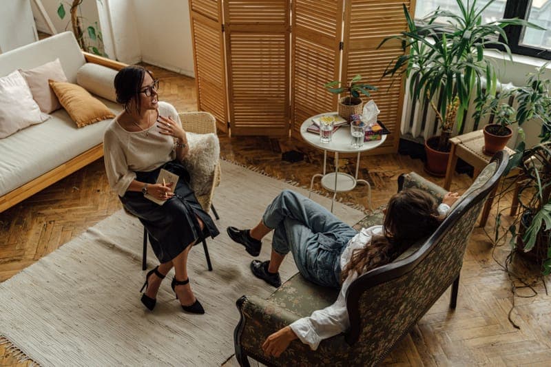 A sunny therapy room with plants, a client lying back while a counsellor listens