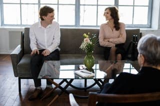 A couple on a grey sofa talking with a therapist in a bright room