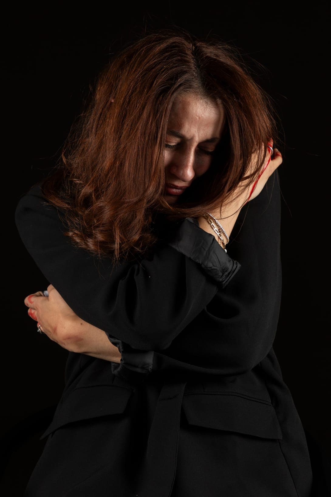 A woman with red hair hugging herself against a black background