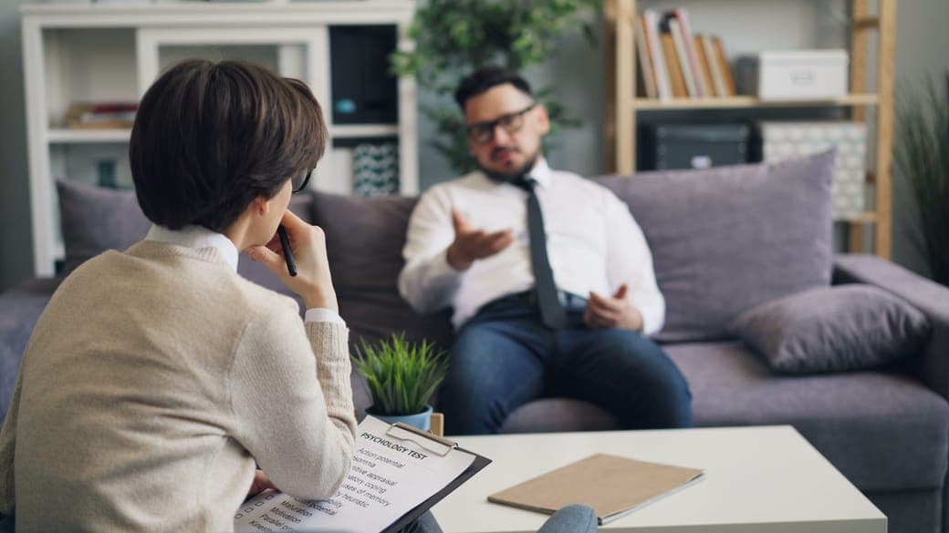 A man in a shirt and tie talking with a counsellor on a purple sofa
