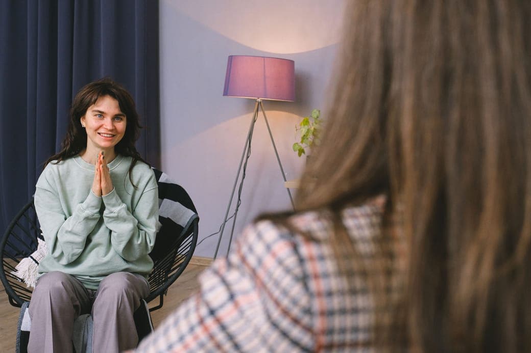 A smiling woman with her hands pressed together, talking with a counsellor