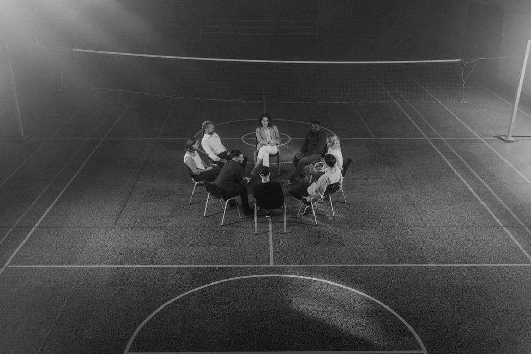 A group sitting in a circle in a large dim hall, seen from above in black and white