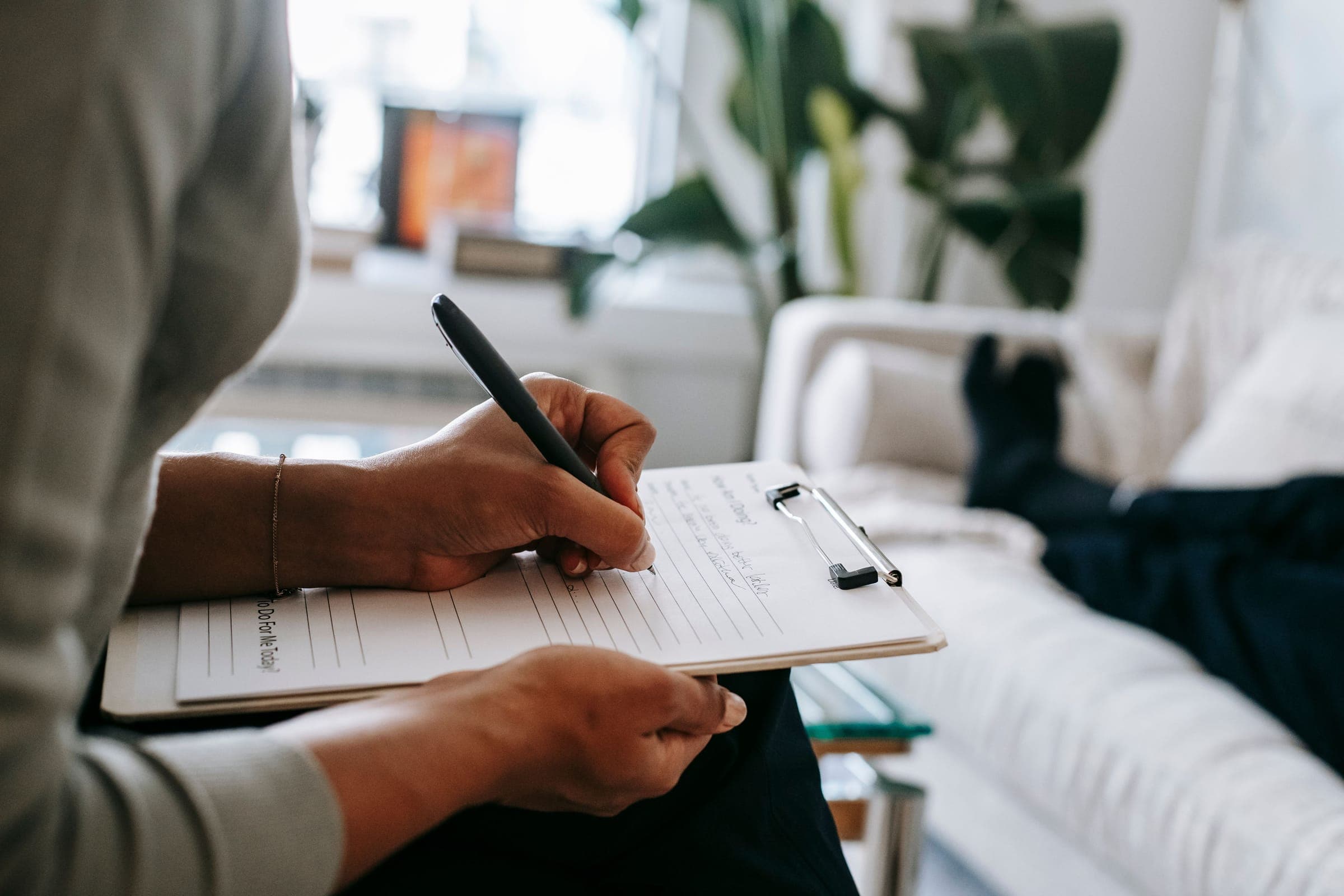 A counsellor writing on a clipboard next to a client resting on a sofa