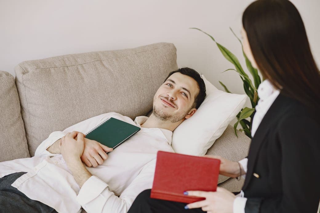 A man lying on a sofa with a book on his chest, talking with a counsellor